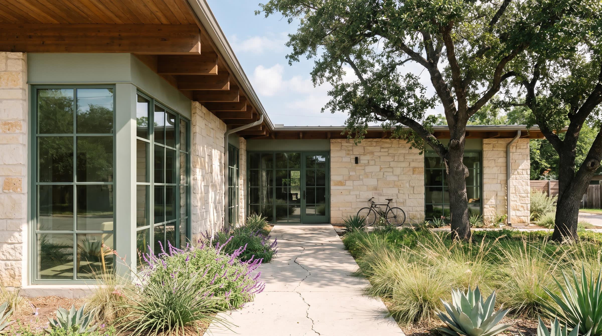 A single-story limestone clinic with live oaks and a concrete walk