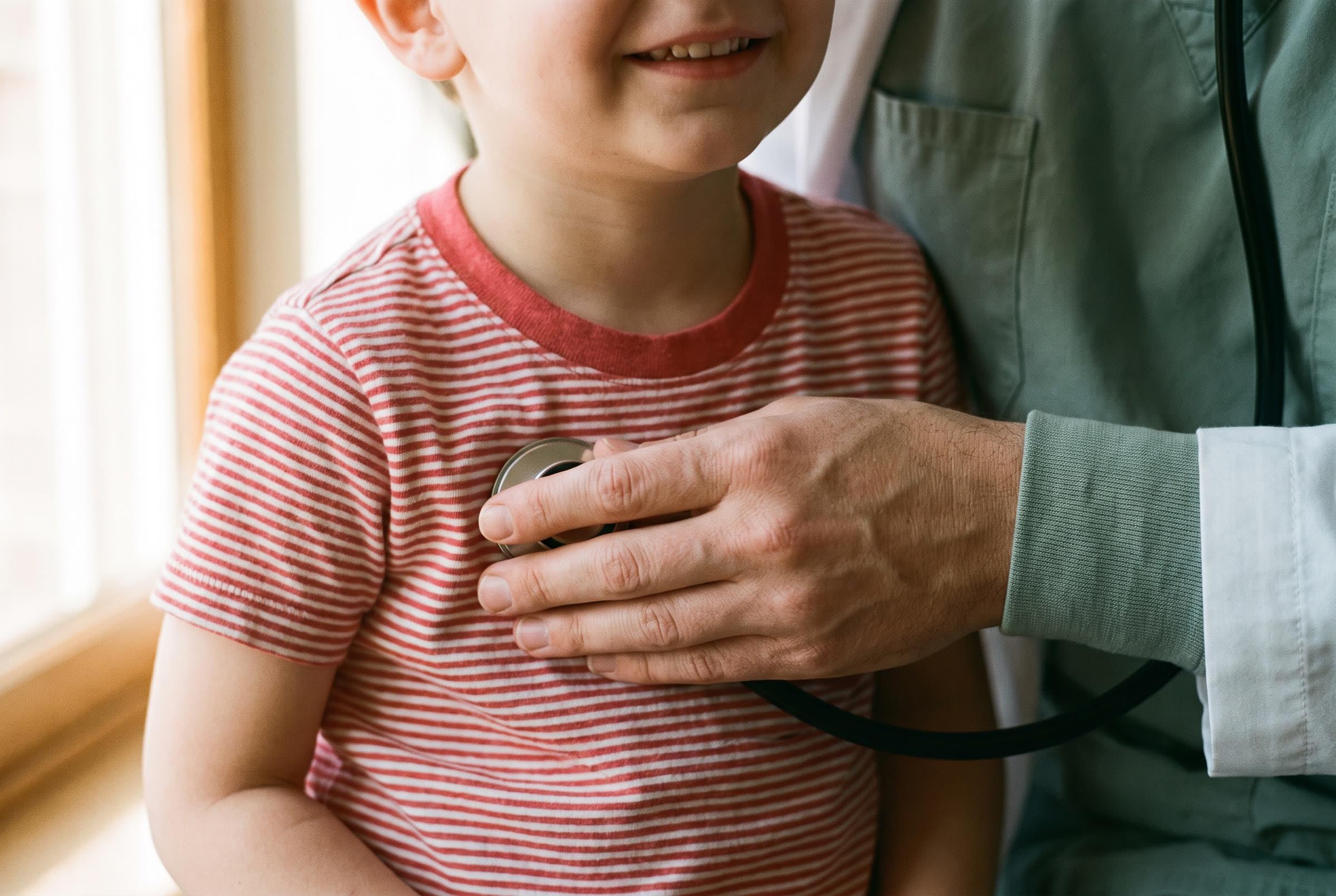 A stethoscope held to a child’s chest, cropped close on the hands