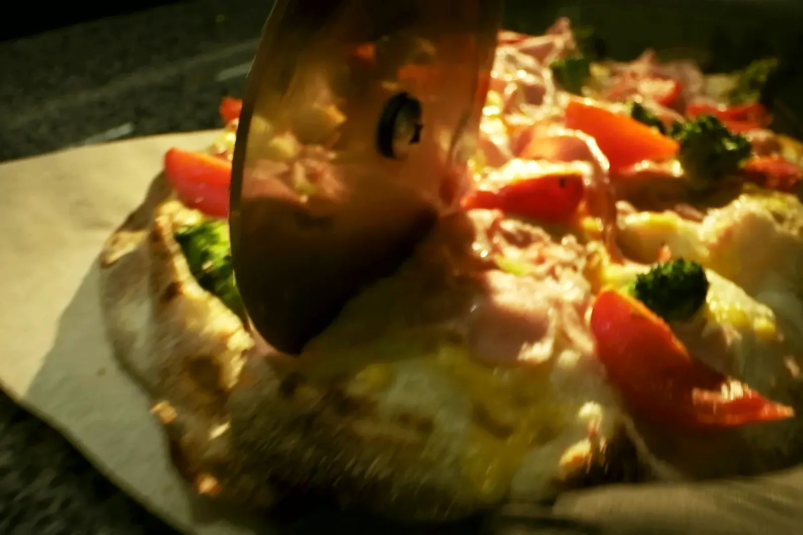 A pizza wheel cutting through a pie topped with tomatoes and broccoli on parchment.