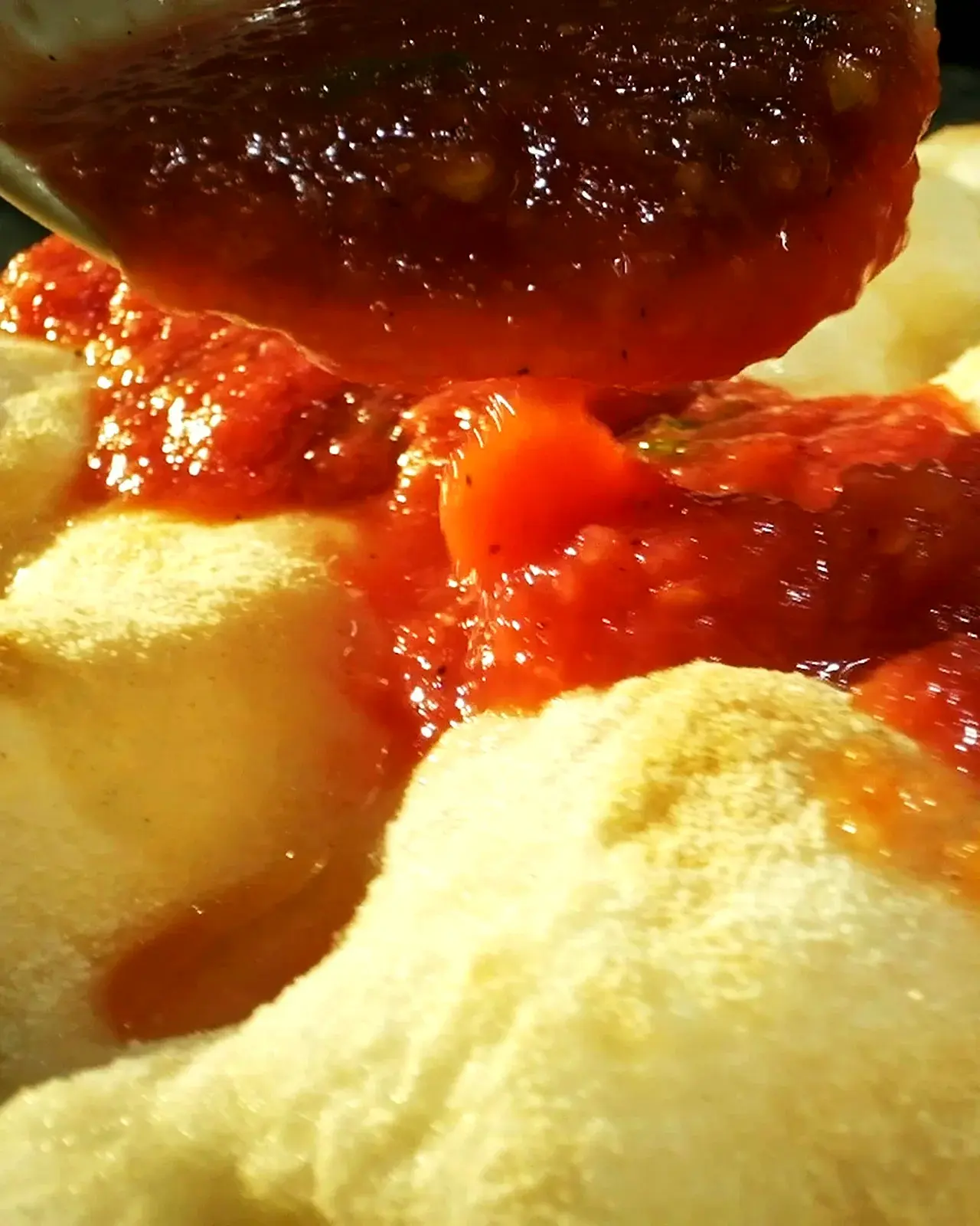 A ladle spooning chunky tomato sauce over a round of puffy pizza dough.
